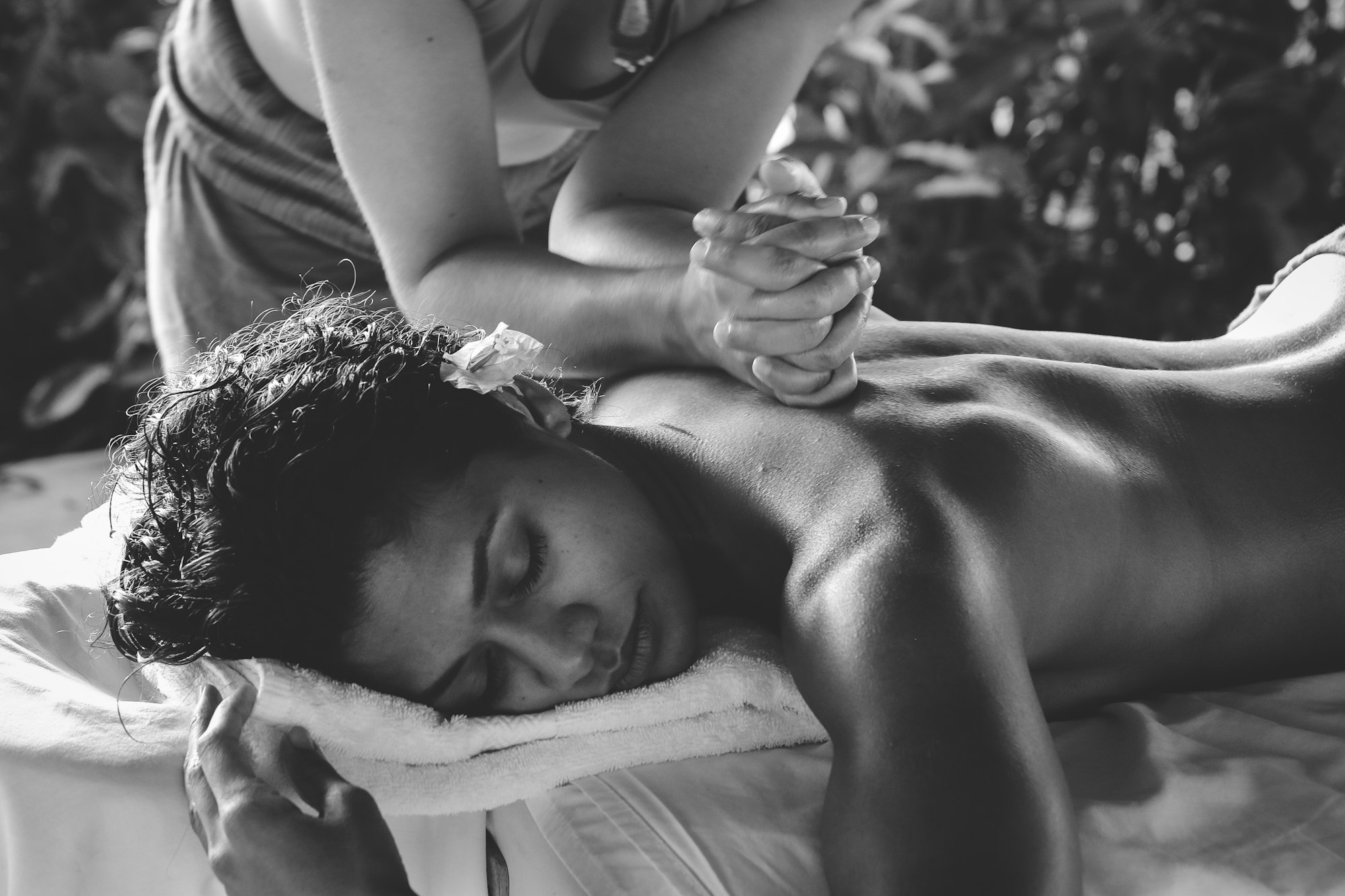 A sports-massage therapist working on a client's back, photographed in black and white
