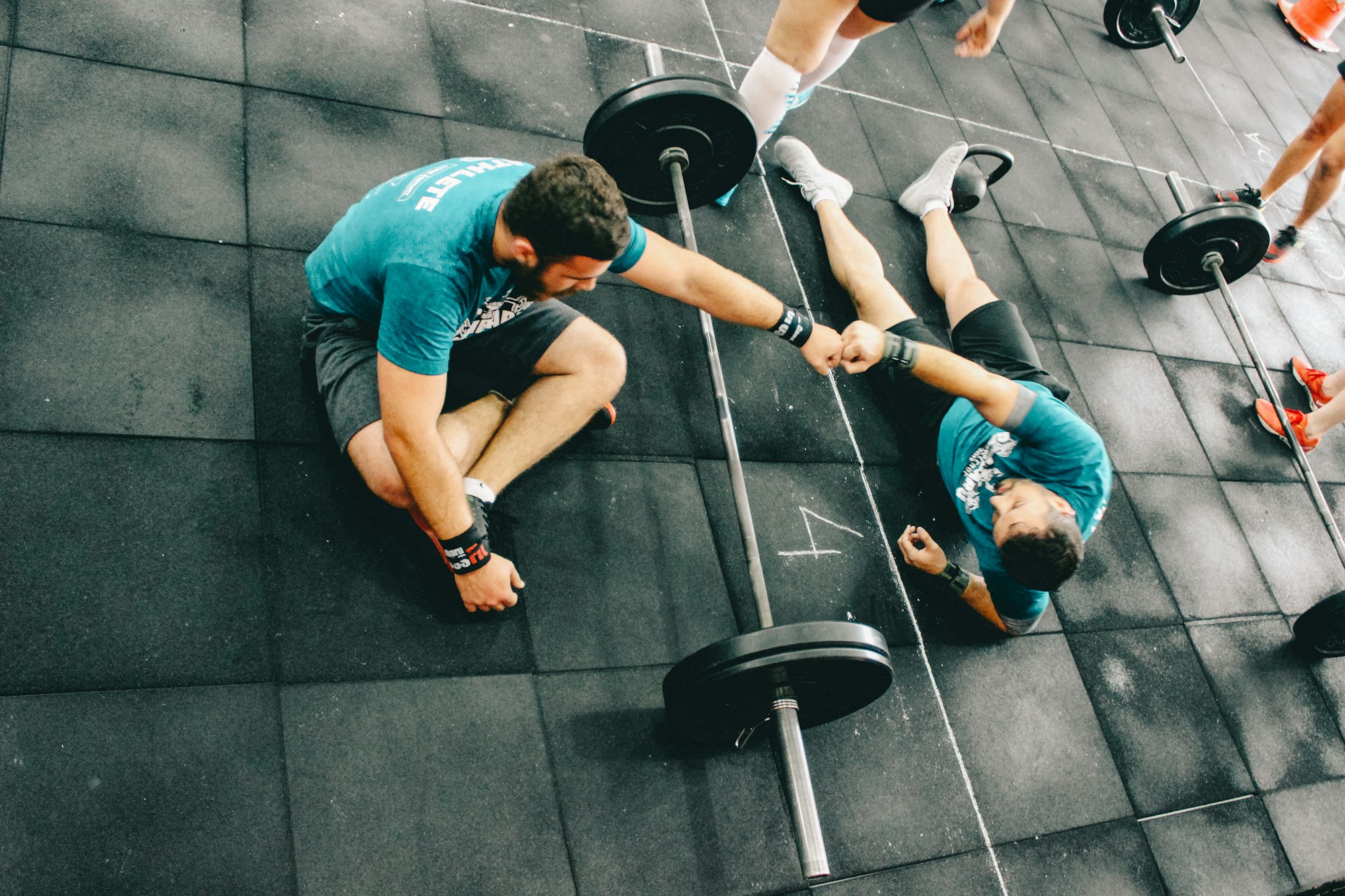 A coach fist-bumping a client who is lying on the gym floor after a set